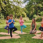 Kinder ueben Yoga im Park mit Trainerin auf Matten im Gruenen.