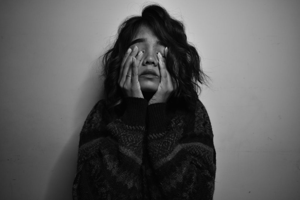 Frau beruehrt ihr Gesicht mit den Haenden in einer intensiven emotionalen Pose.