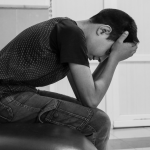 Junge sitzt mit gesenktem Kopf und haelt den Kopf in den Haenden vor Stress.