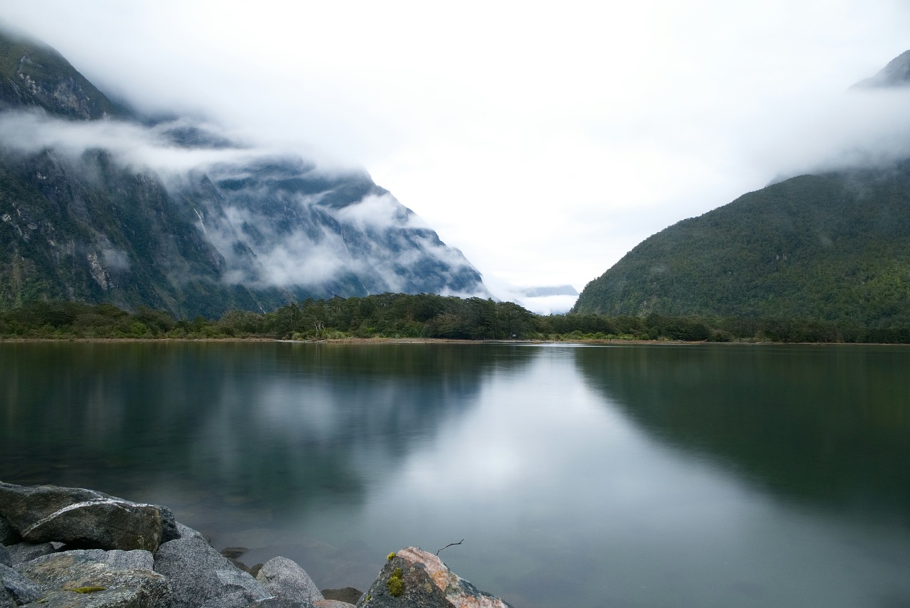 Nebeliger Bergsee mit Spiegelung, umgeben von Bergen und stiller Natur